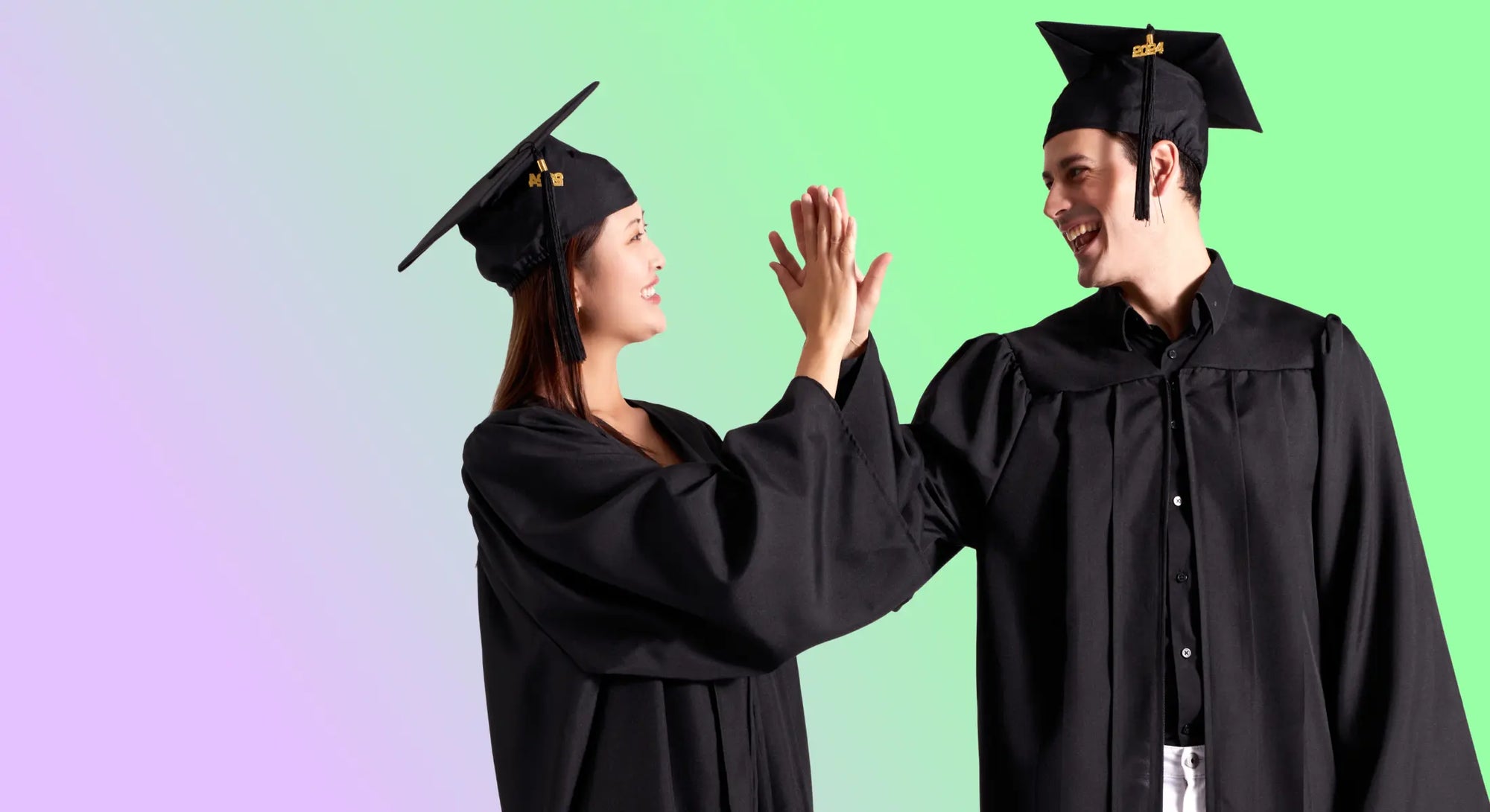 Male and female graduates wearing gowns and caps celebrate graduation with a high five.